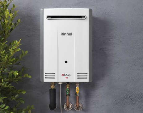White Rinnai wall-mounted water heater with exposed pipes on a gray wall White Rinnai wall-mounted water heater with exposed pipes on a gray wall