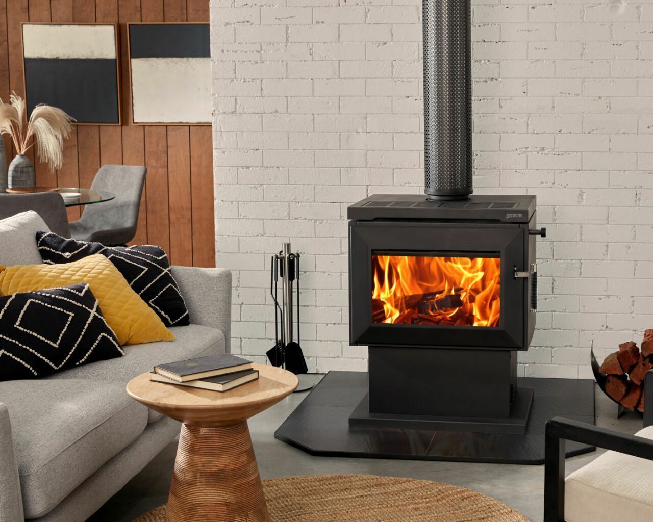 Modern living room with a lit black wood stove, gray sofa, and wooden side table.