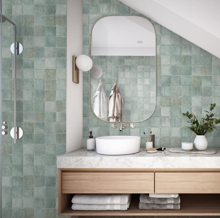 Modern bathroom with pale green tile, round mirror, white sink, wood vanity, and plants Modern bathroom with pale green tile, round mirror, white sink, wood vanity, and plants