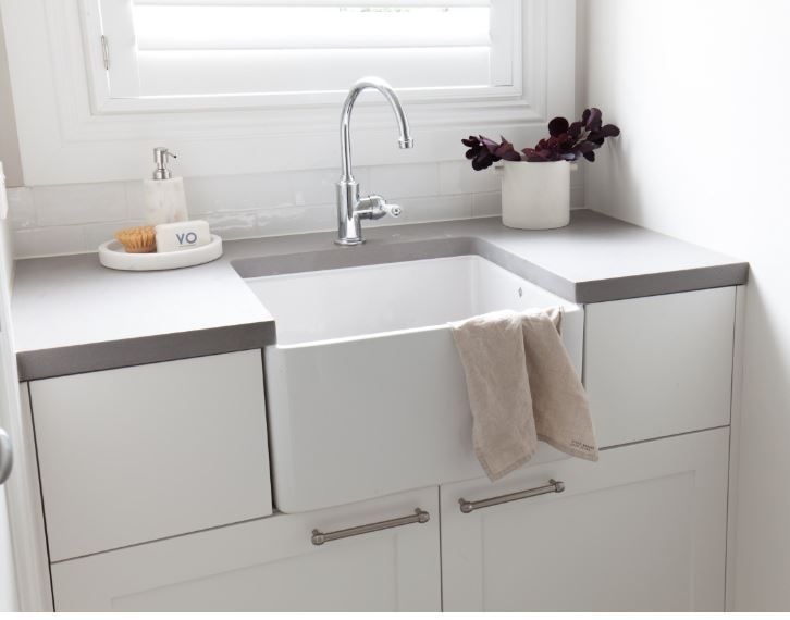 White farmhouse sink in a bright kitchen with gray countertops, faucet, towels, and a potted plant by the window