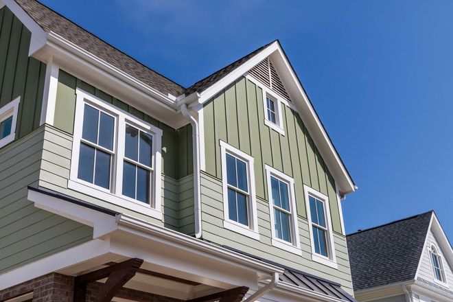 Close-up of a green house exterior with white-trimmed windows and a steep roof against a blue sky