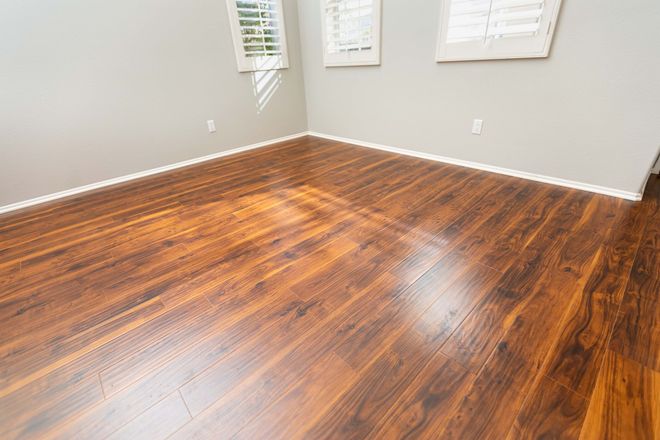 Empty room with glossy dark hardwood floors and light gray walls, lit by daylight from windows.