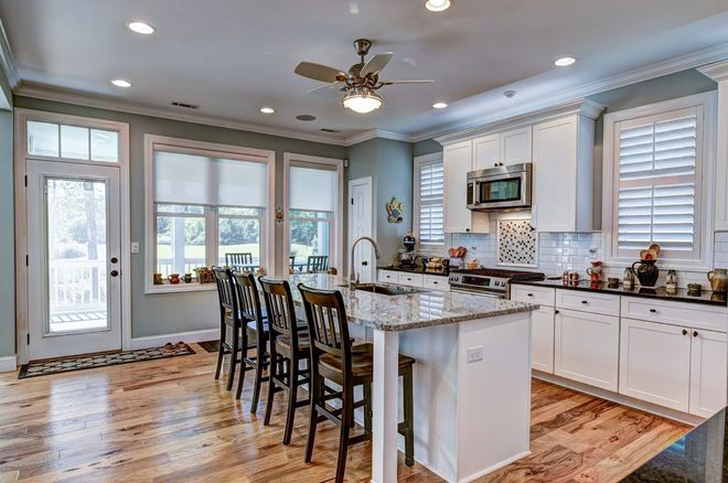 Bright kitchen with island seating, white cabinets, granite counters, and large windows.
