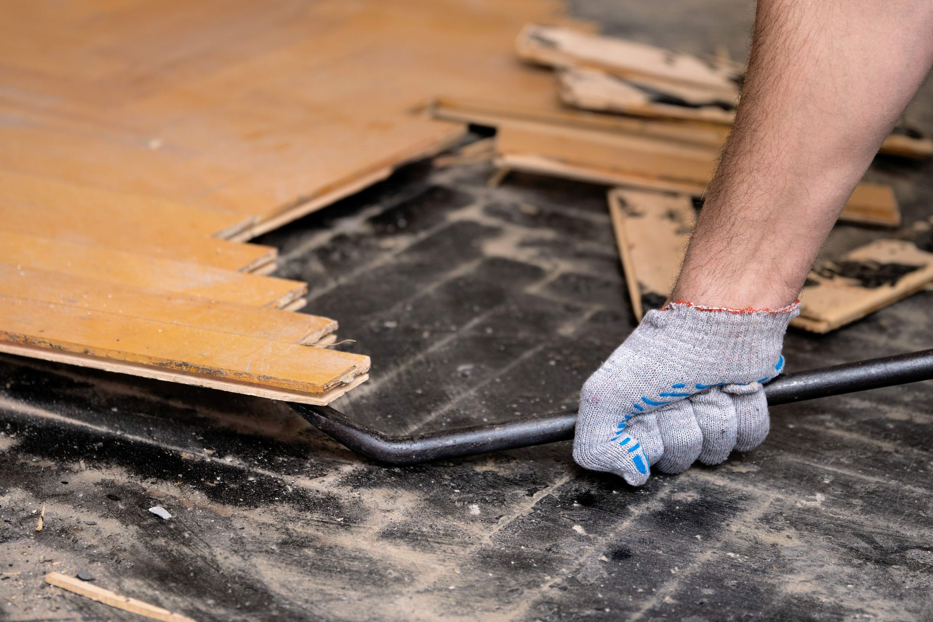 Gloved hand prying up old wooden flooring with a crowbar during renovation Gloved hand prying up old wooden flooring with a crowbar during renovation