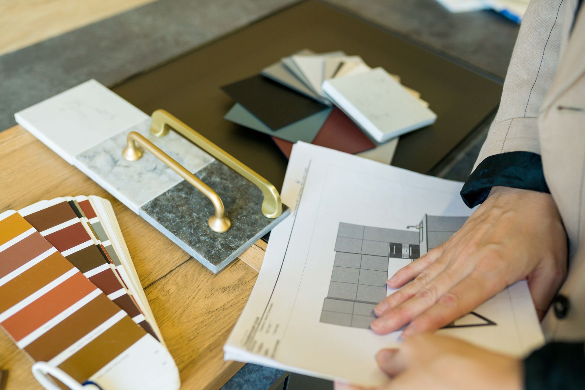 Person reviewing paint swatches and a flooring sample on a desk with design plans Person reviewing paint swatches and a flooring sample on a desk with design plans