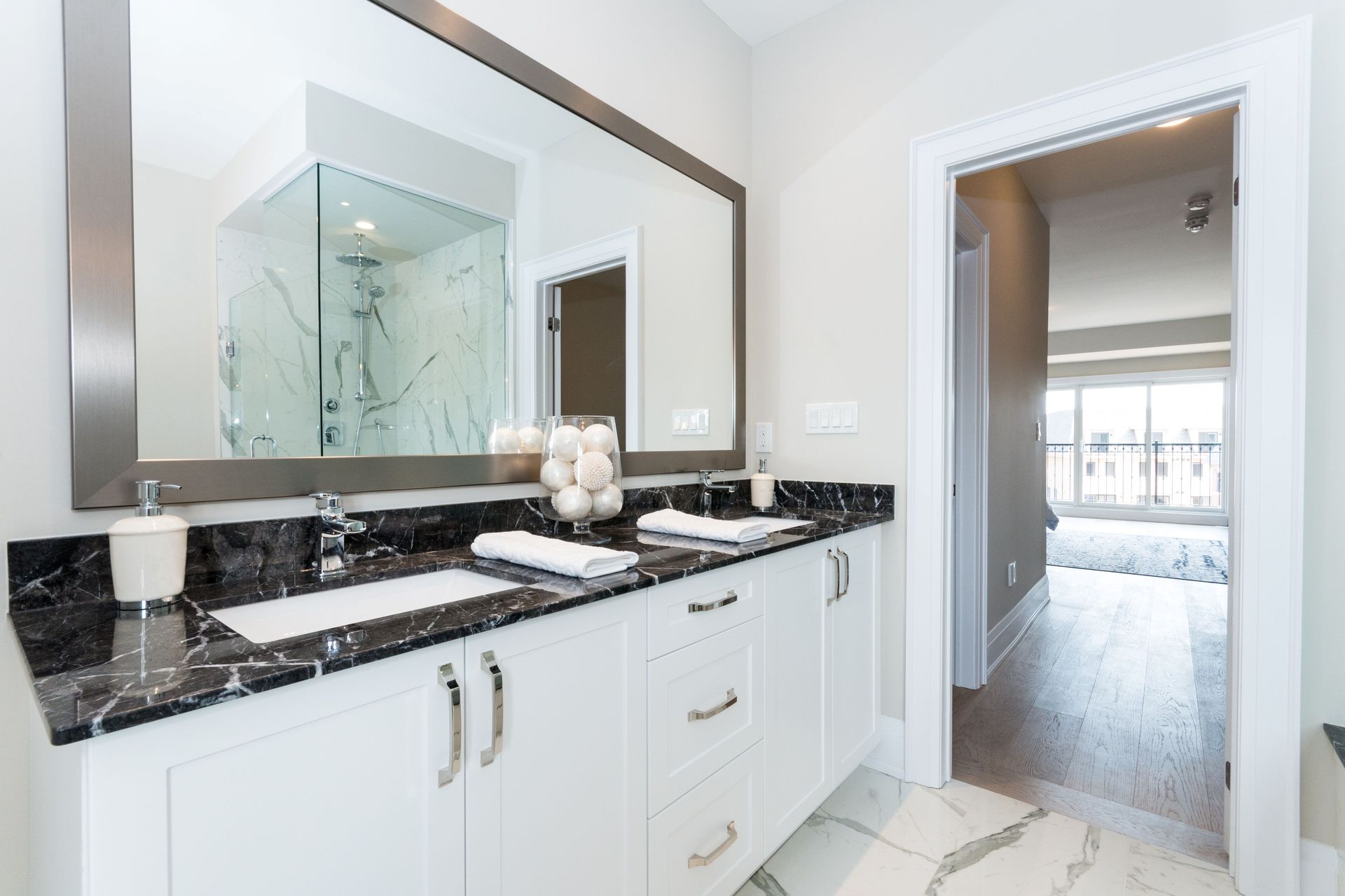 Bright modern bathroom vanity with black countertop, white cabinets, and large wall mirror Bright modern bathroom vanity with black countertop, white cabinets, and large wall mirror