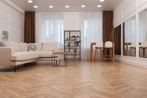 Bright modern living room with sofa, coffee table, dining set, and herringbone wood floor