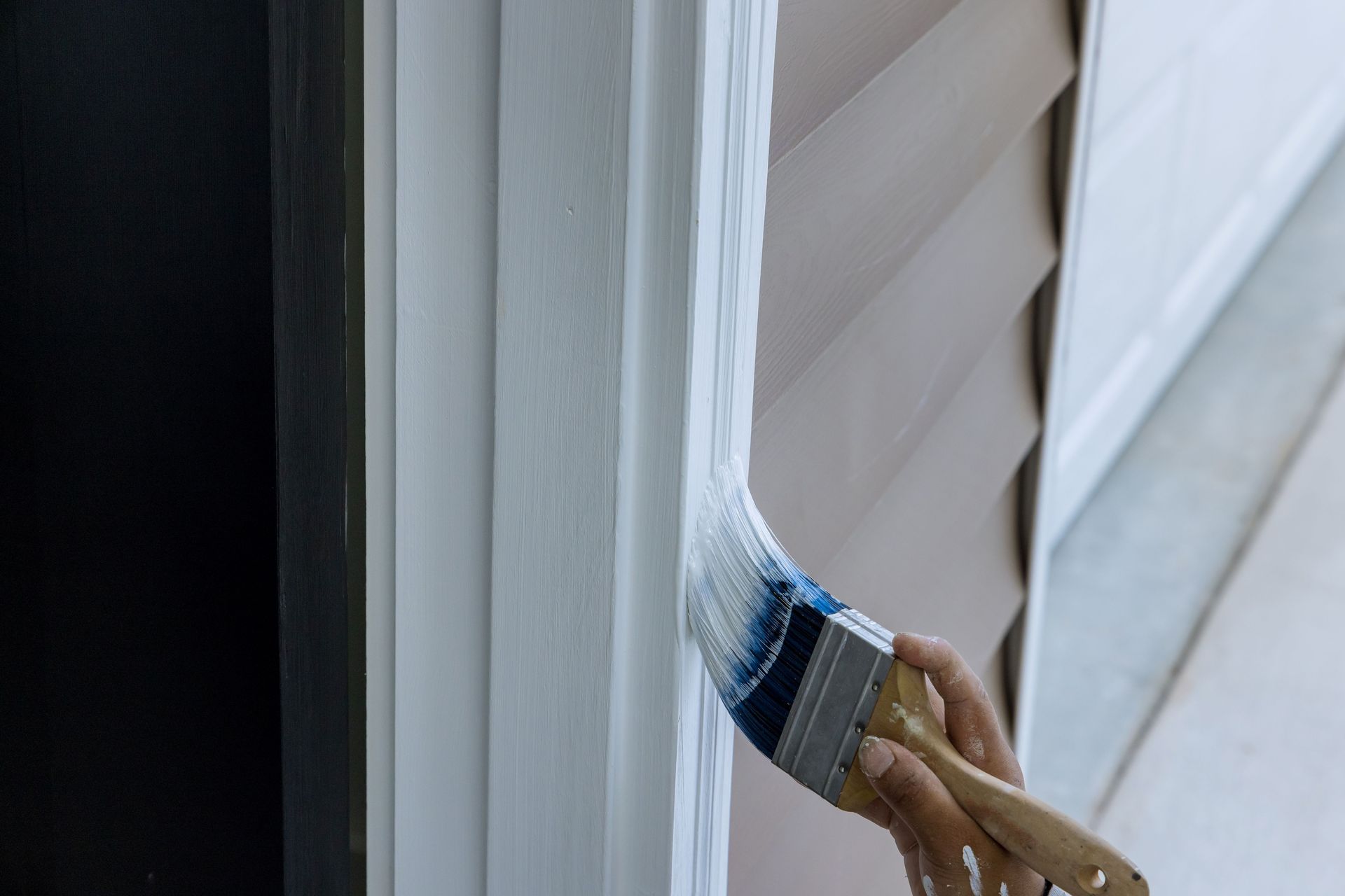Paintbrush painting white trim around a window frame outdoors Paintbrush painting white trim around a window frame outdoors