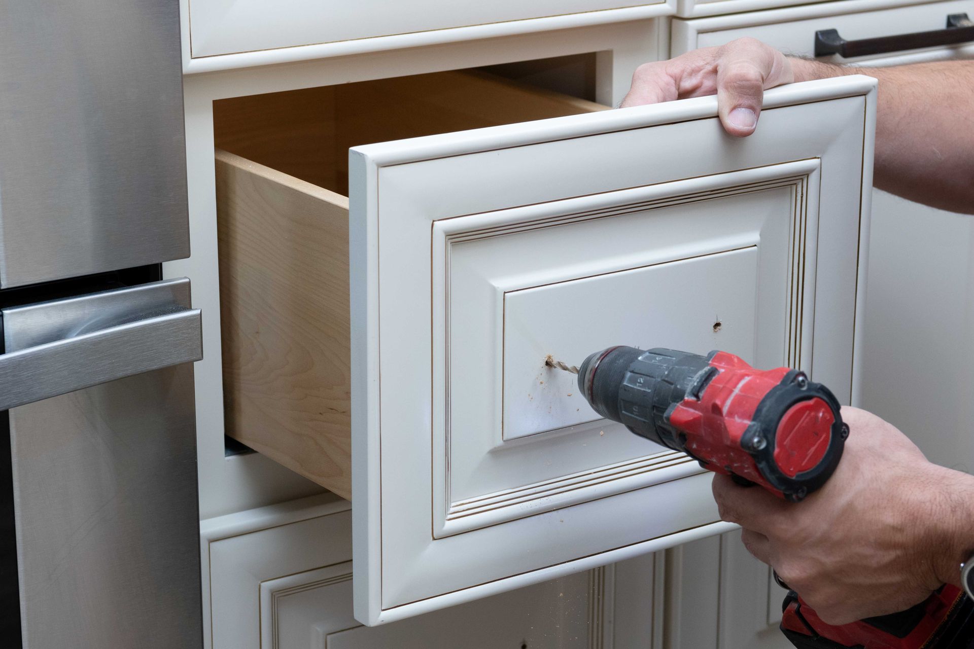 Hand drilling a white cabinet drawer front with the drawer open Hand drilling a white cabinet drawer front with the drawer open