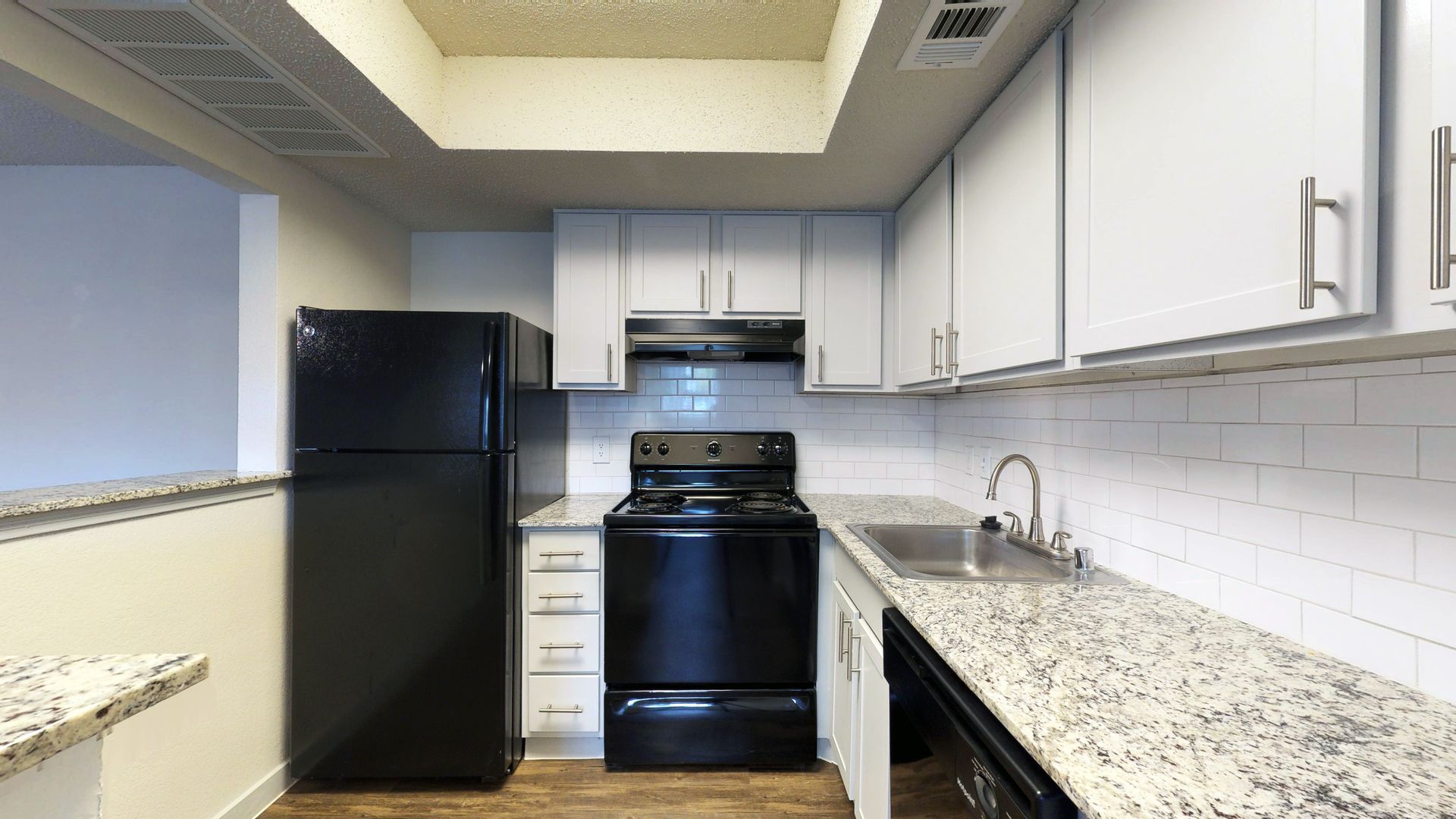 Bright kitchen with white cabinets, black appliances, and speckled countertops