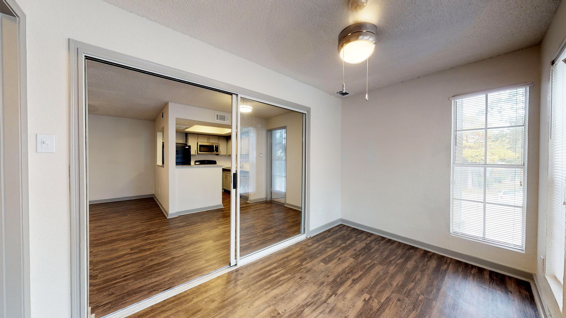 Bright empty room with wood floors, mirrored closet doors, ceiling fan, and window blinds.