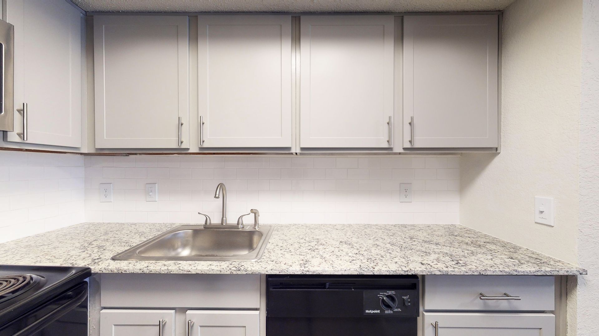 Modern kitchen with white cabinets, speckled countertop, stainless sink, and built-in stove.