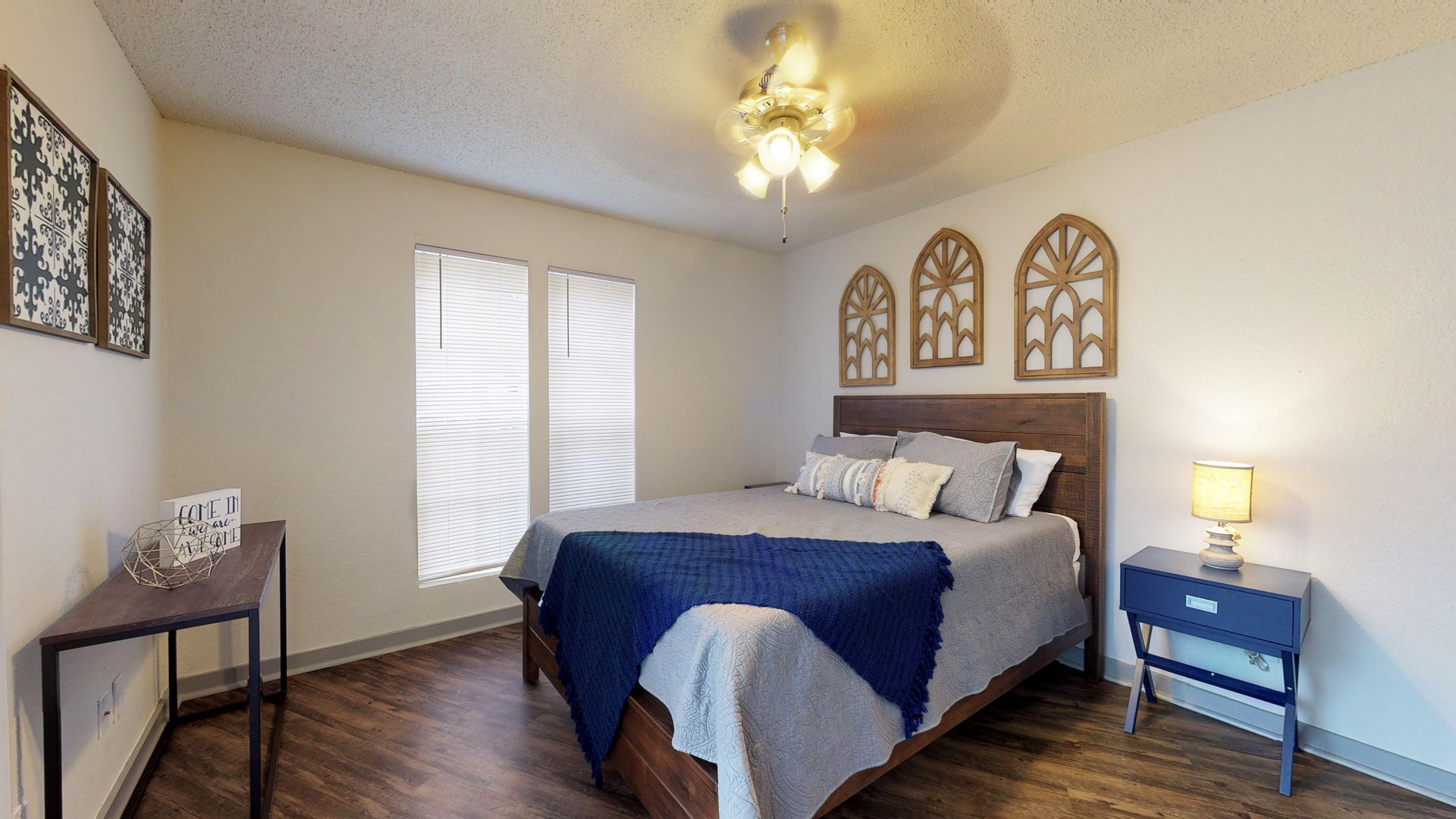 Cozy bedroom with a blue bedspread, nightstand lamps, wall decor, and wood flooring