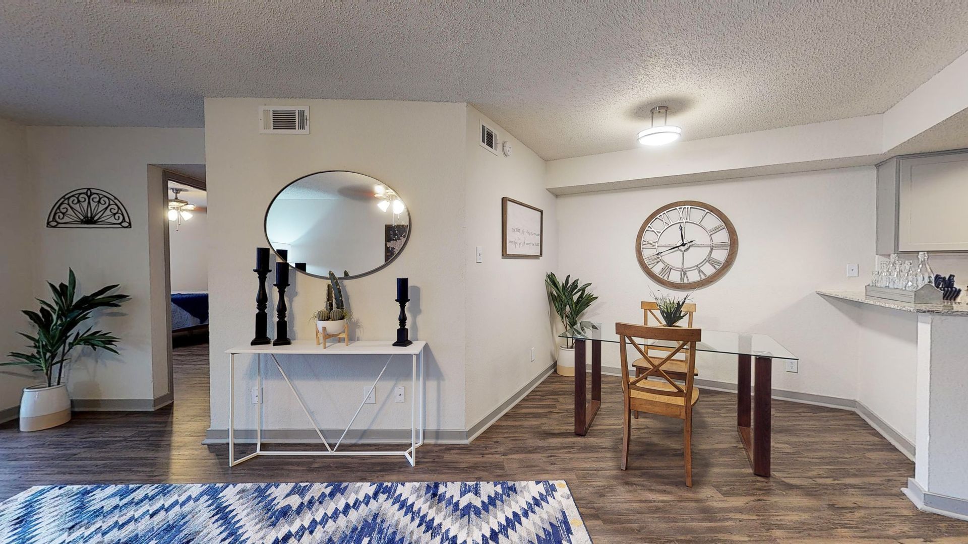 Bright open dining area with wooden table, wall mirror, plants, and blue patterned rug in a modern home