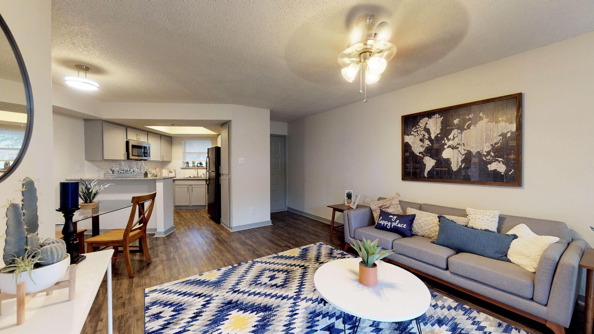Bright living room with gray sofa, blue patterned rug, round white coffee table, and open kitchen view