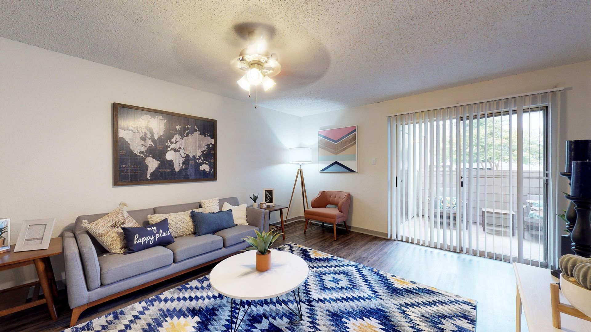 Bright living room with gray sofa, blue patterned rug, round coffee table, chair, and sliding glass doors