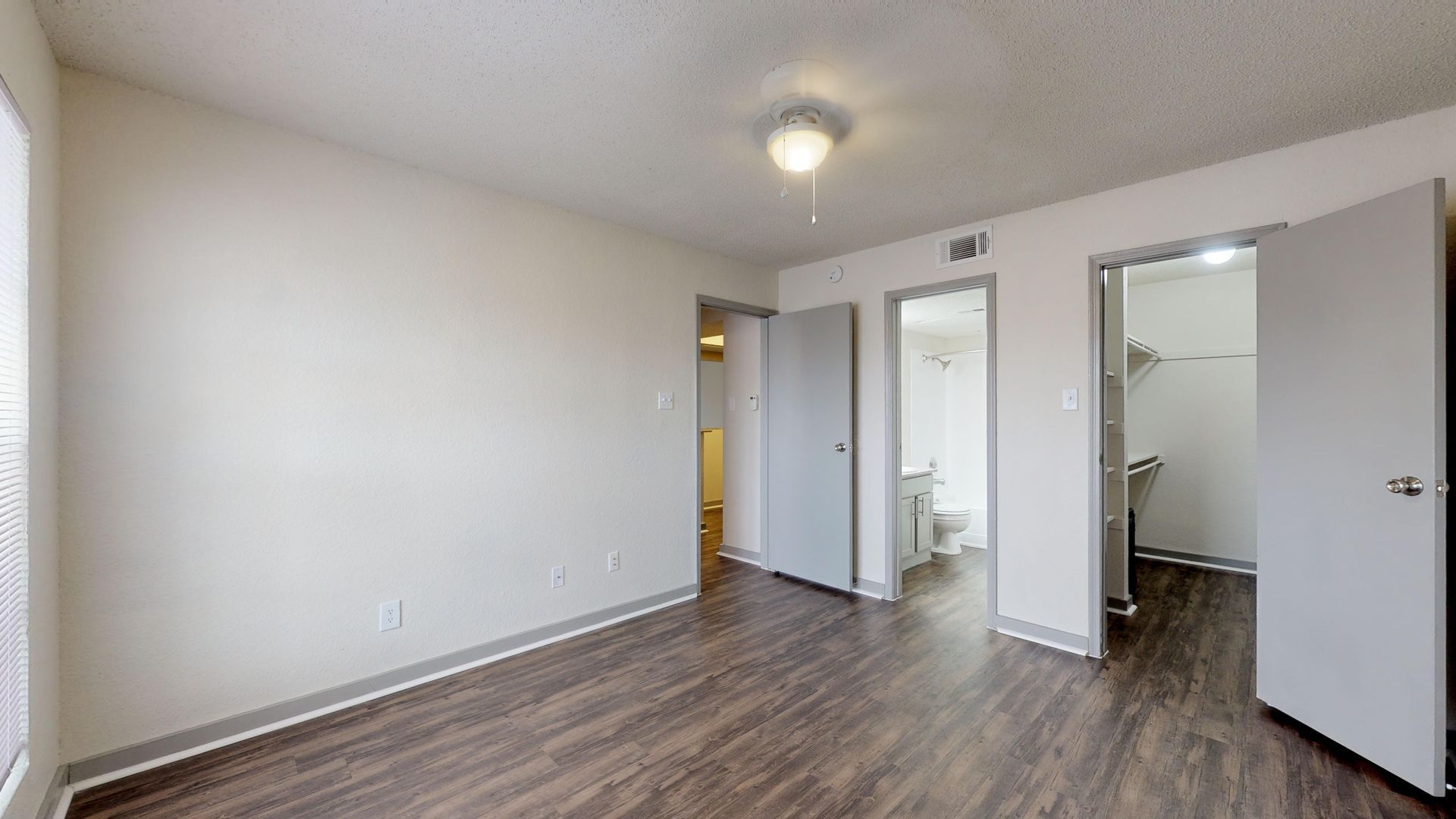 Empty bedroom with wood floors, white walls, and open closet and bathroom doors