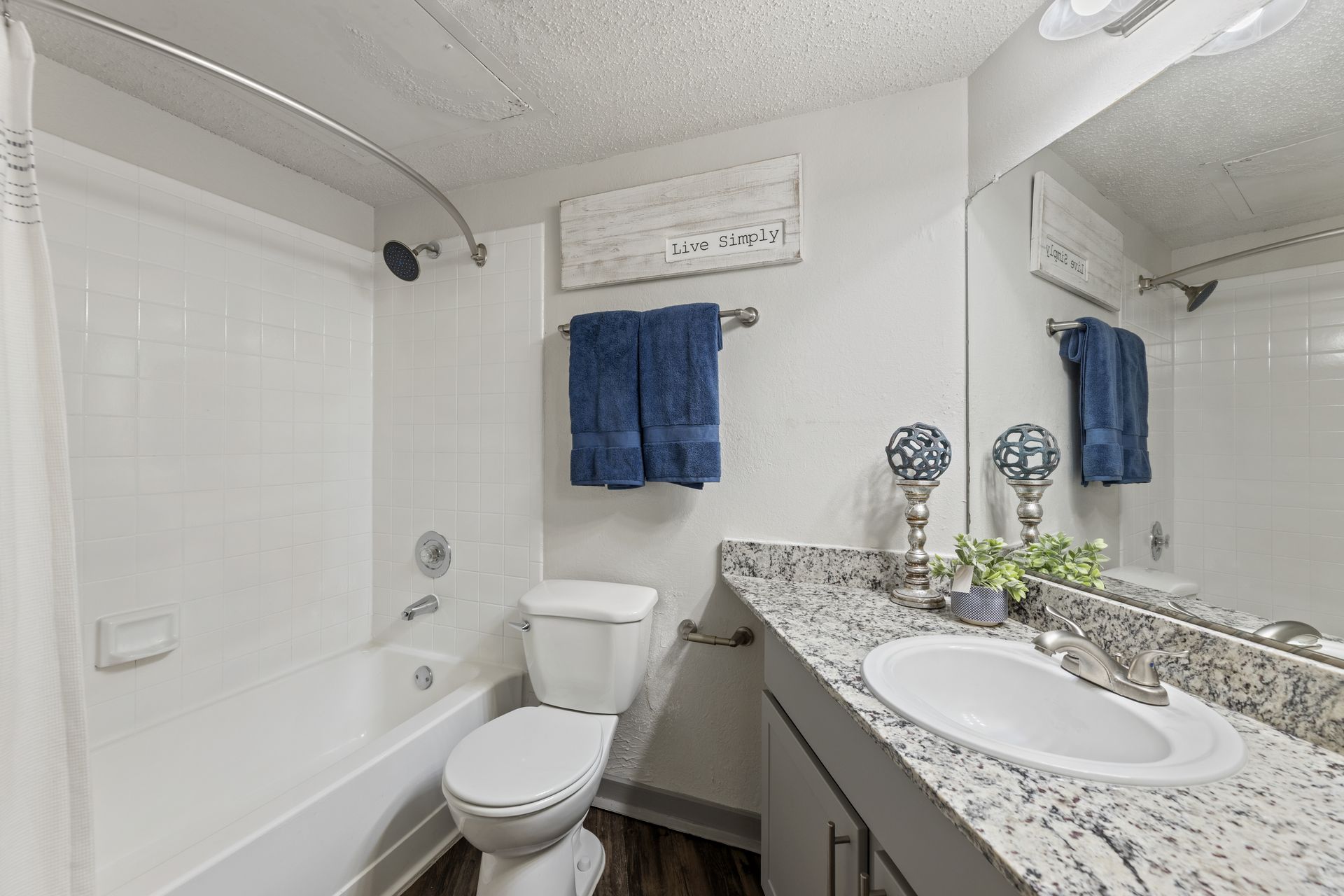 Bright white bathroom with tub, toilet, granite vanity, and blue towels