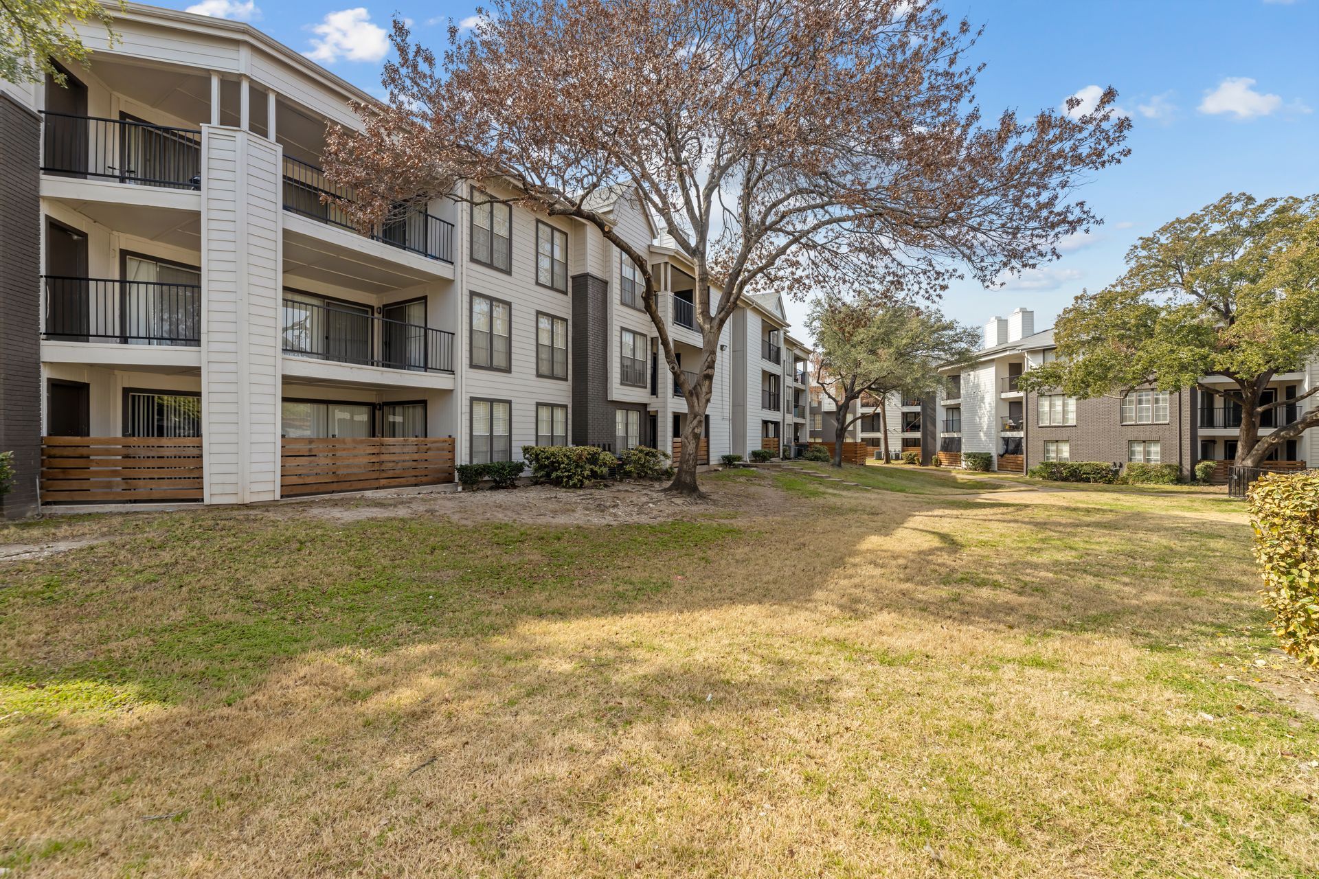 Apartment complex with balconies facing a grassy courtyard and large trees