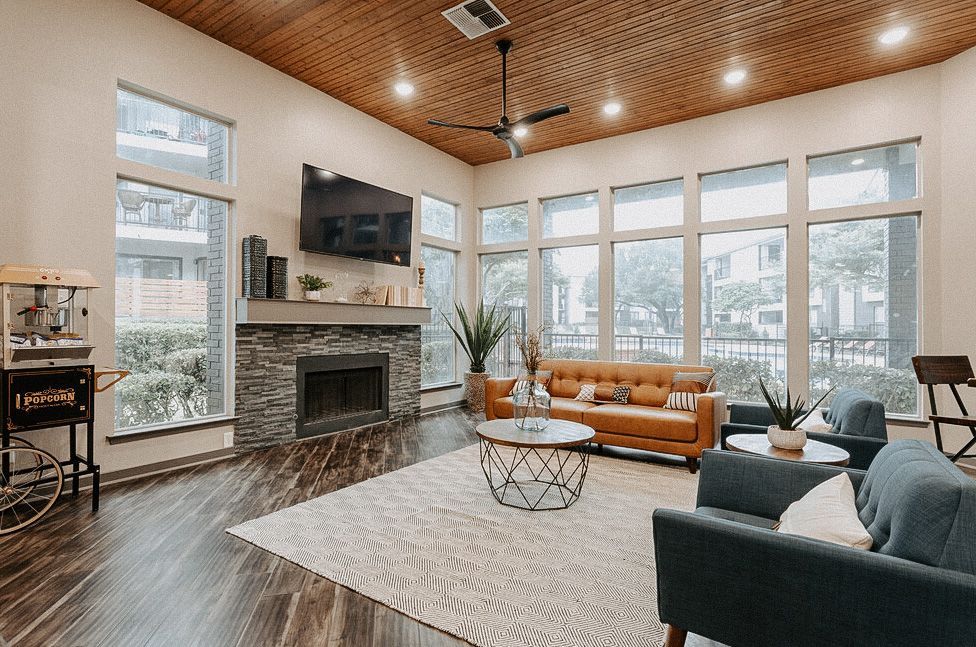 Modern living room with fireplace, large windows, tan sofa, gray chair, and wood ceiling