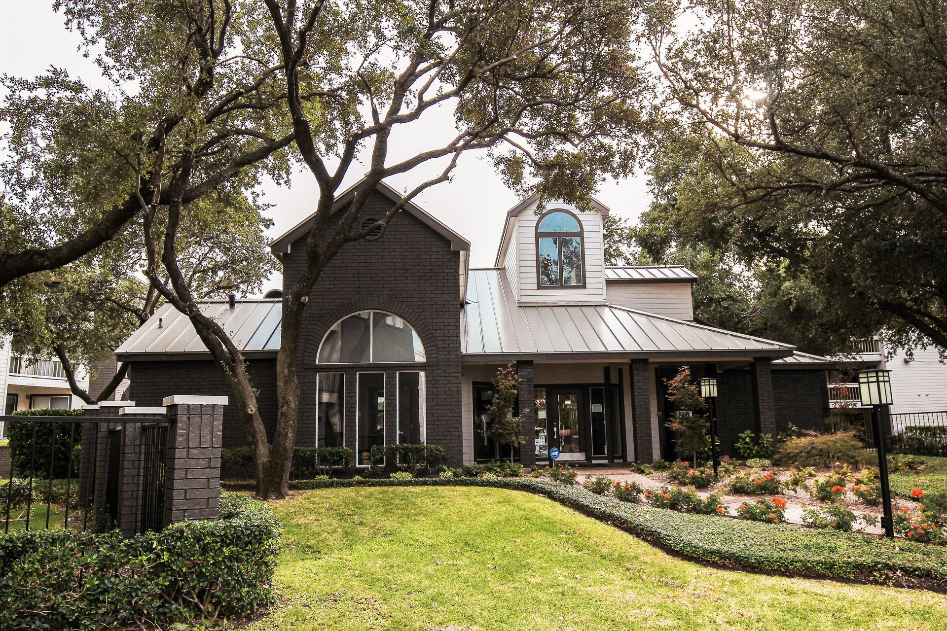 Dark gray house with arched windows, a landscaped lawn, and large trees in front