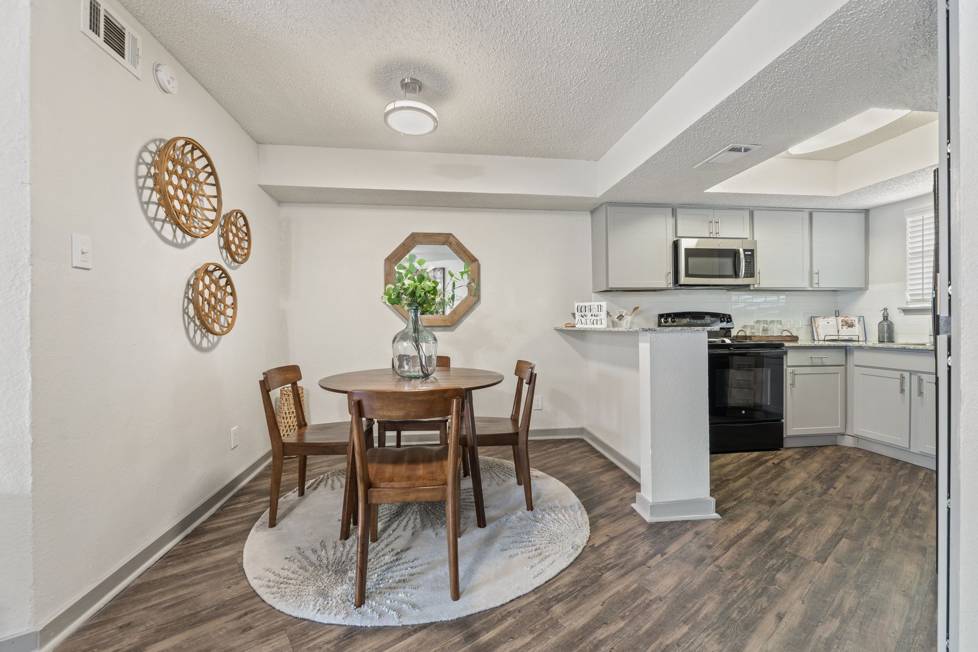 Bright dining area with wooden table and chairs beside a white kitchen and dark wood flooring.