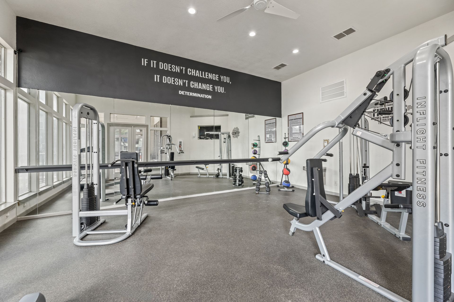 Bright gym interior with cable machines, benches, and gray carpet under high ceilings