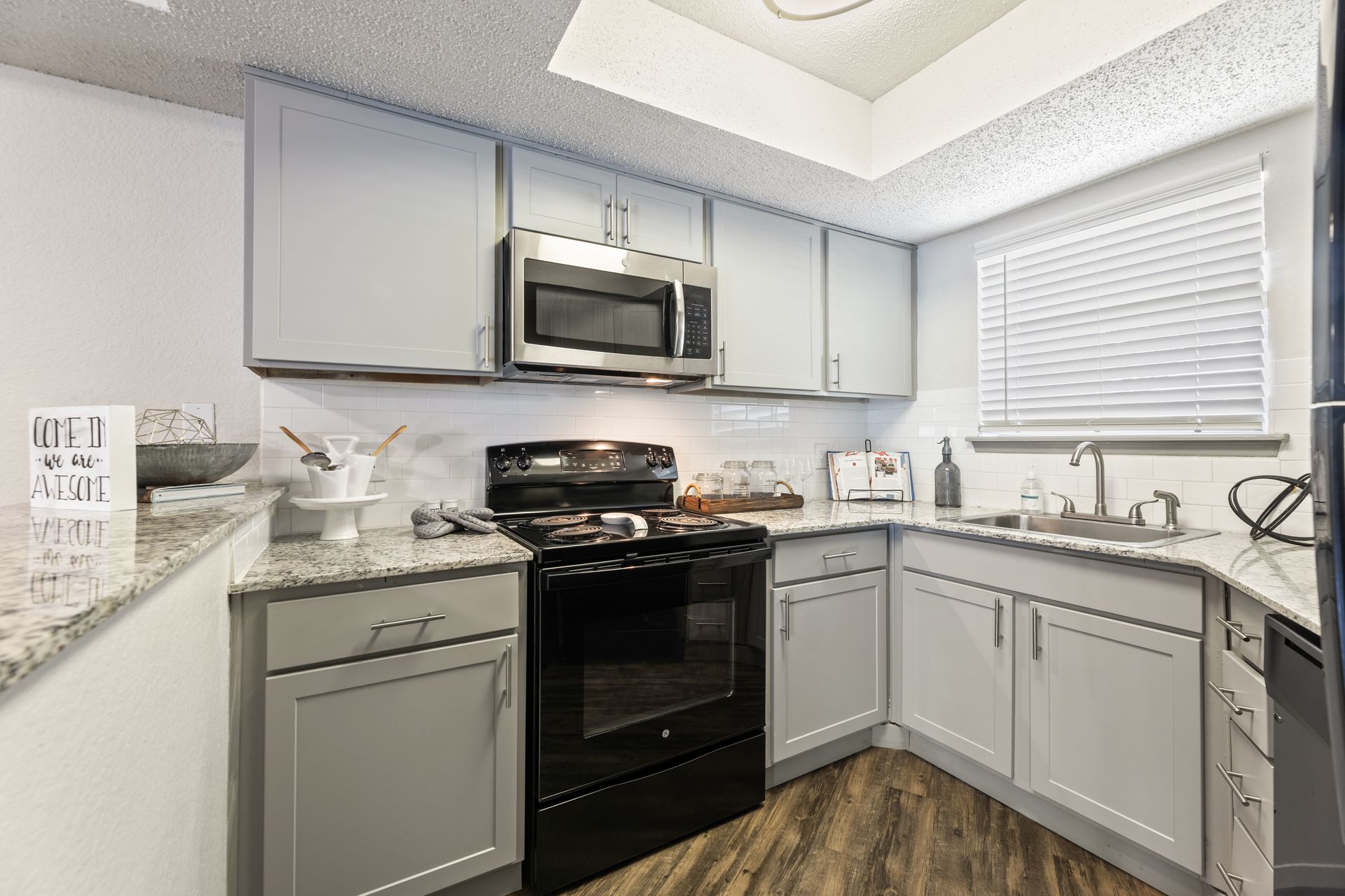 Bright modern kitchen with gray cabinets, black stove, and stainless steel microwave.