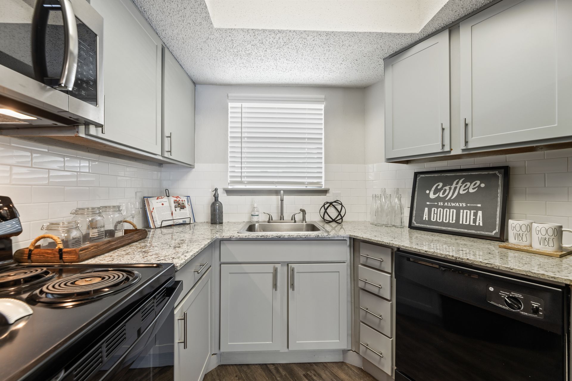 Compact gray kitchen with white tile backsplash, black appliances, and a window above the sink