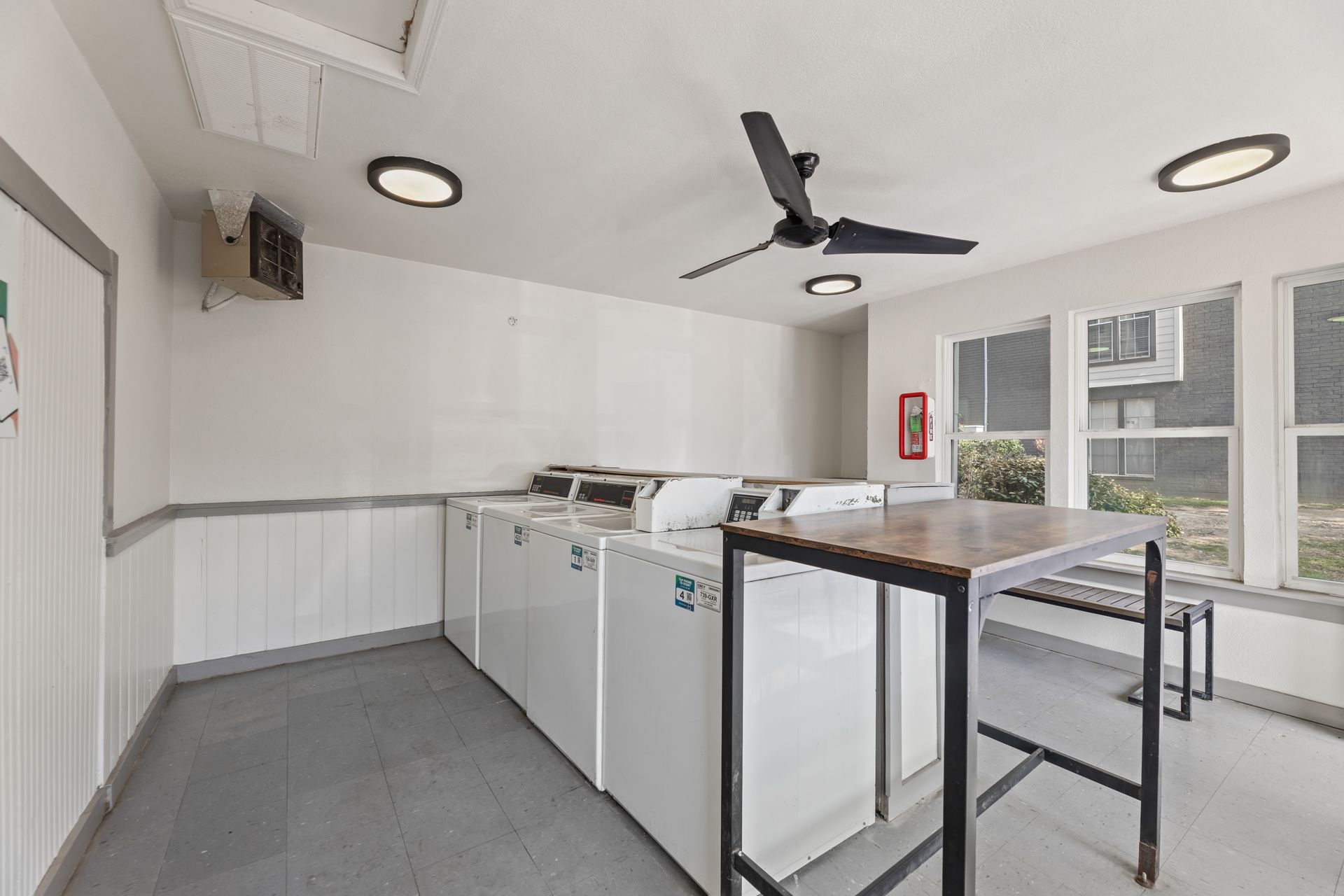 Bright laundry room with white cabinets, washer, sink, ceiling fan, and large windows.