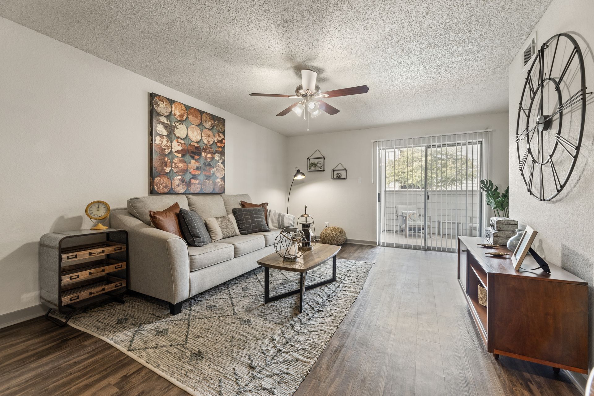 Bright living room with gray sofa, coffee table, wall art, large wall clock, and sliding glass door.