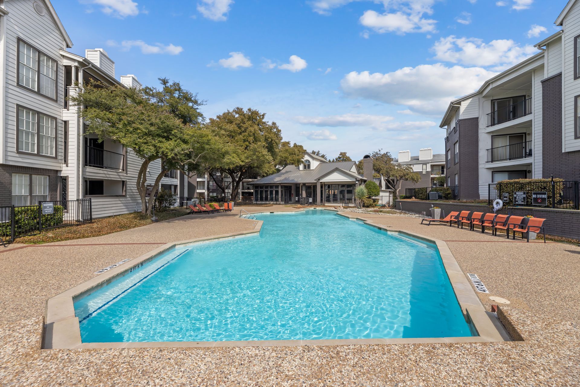 Apartment complex courtyard with a turquoise swimming pool and lounge chairs under a blue sky