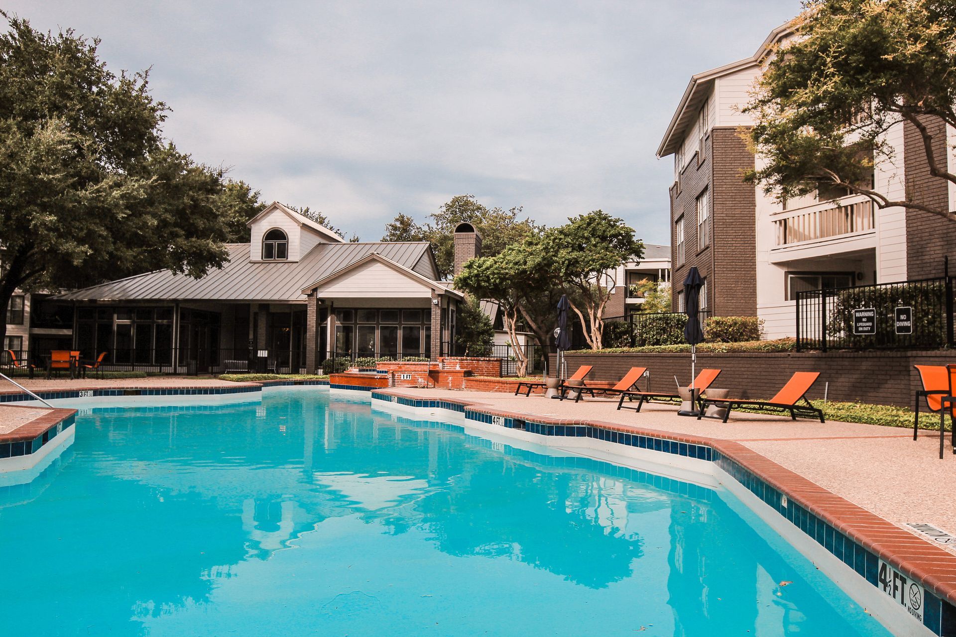 Outdoor swimming pool with orange lounge chairs beside apartment buildings and trees