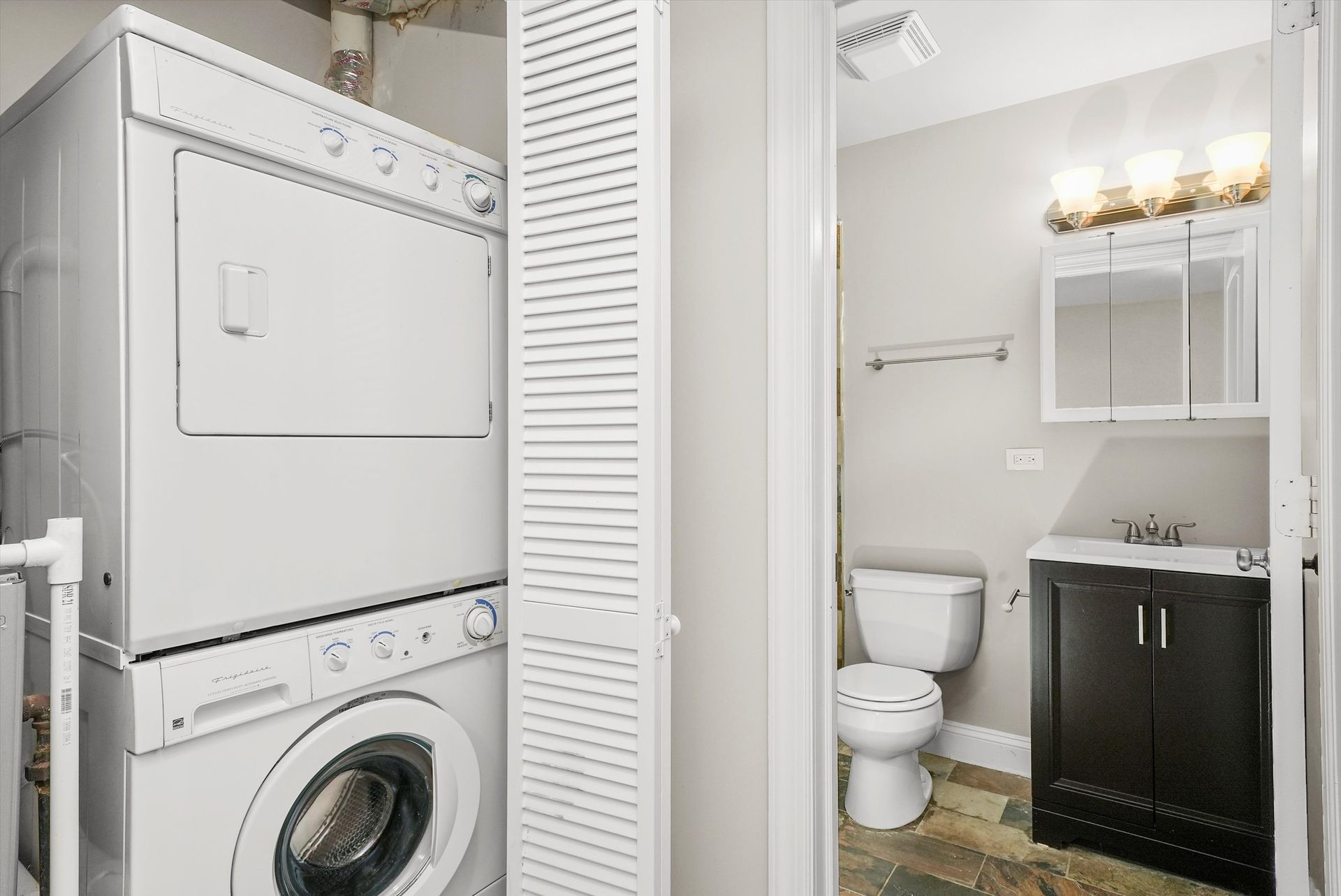 Stacked washer/dryer next to a bathroom with a toilet, sink, and mirror.