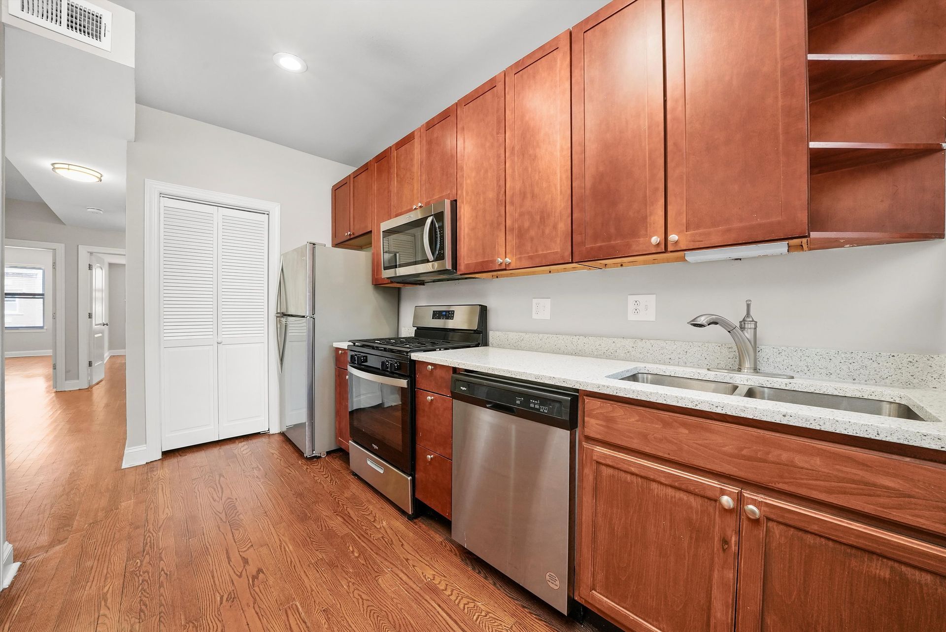 Kitchen with wooden cabinets, stainless steel appliances, and a view of a hallway.