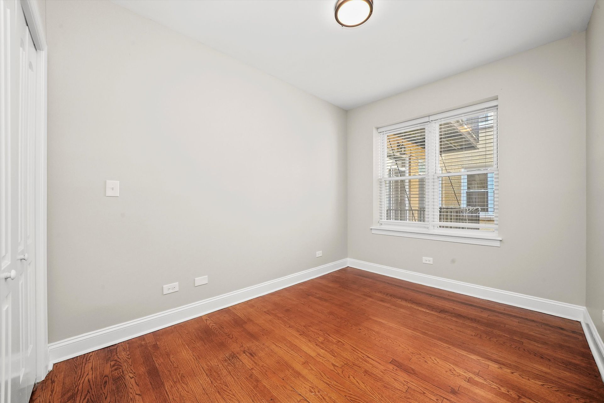 Empty room with wood floor, window, and white walls.
