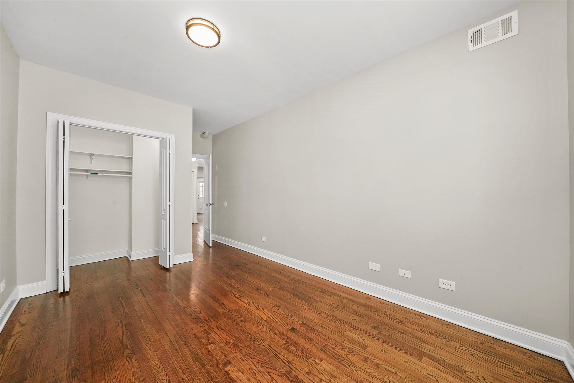Empty bedroom with hardwood floors, closet, and neutral-colored walls.