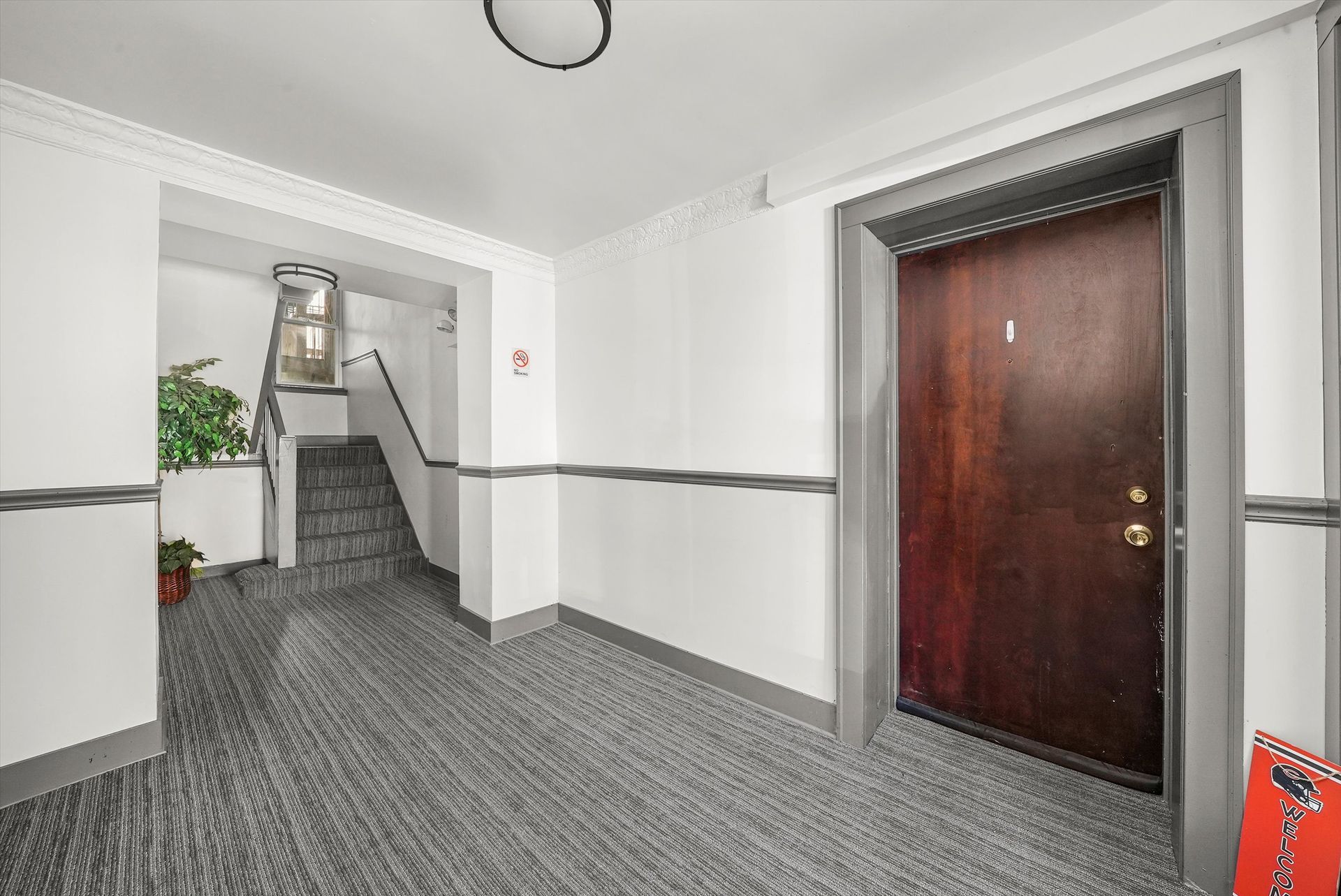 Hallway with a brown door, gray trim, stairs, and patterned carpet.