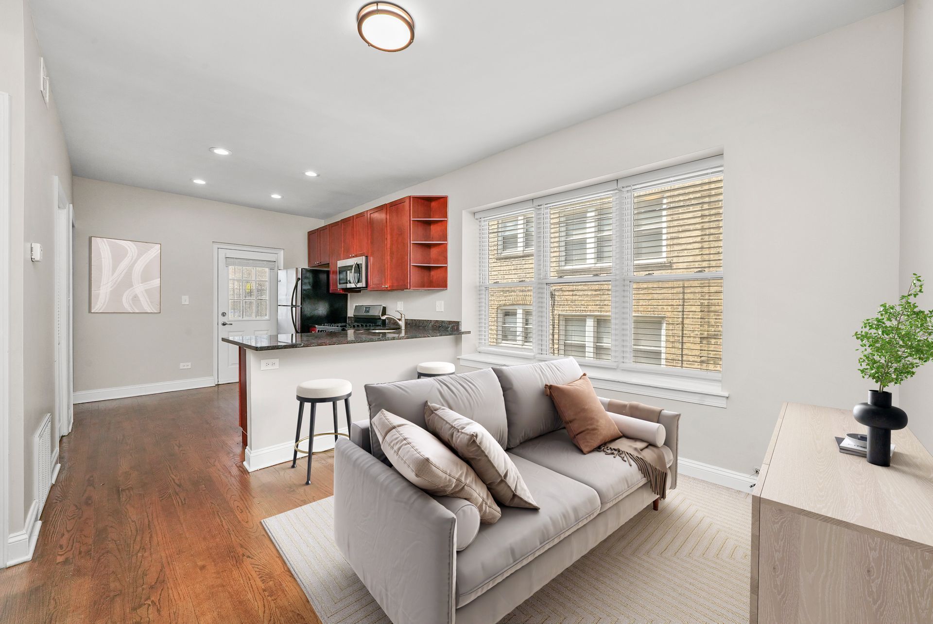 Cozy living space with gray sofa, open kitchen with red cabinets, and hardwood floors.