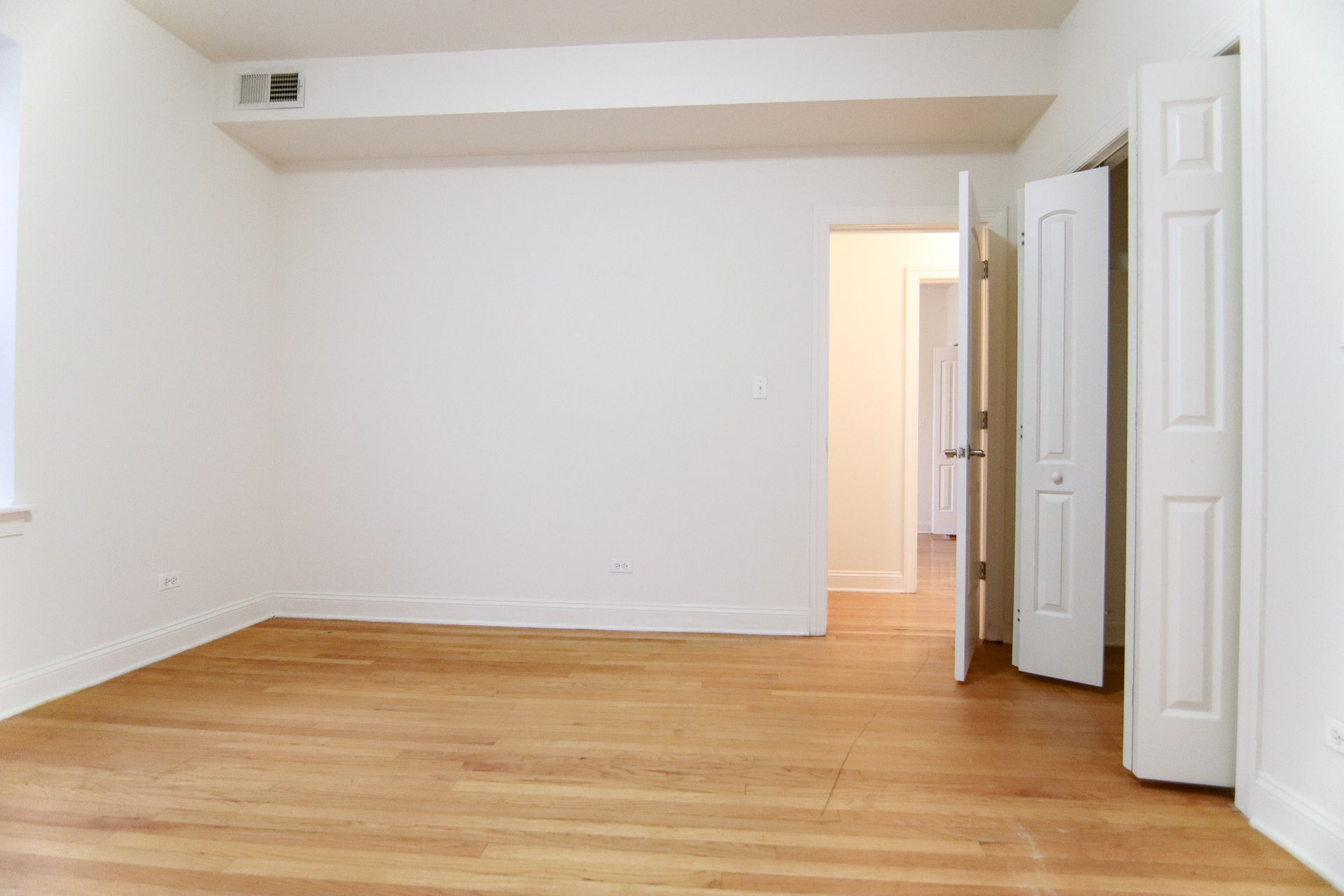 Empty room with hardwood floors, white walls, and an open closet.