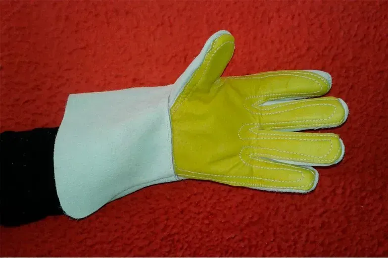 Una mano que lleva un guante de trabajo de cuero amarillo con un puño protector blanco largo, sobre un fondo rojo texturizado.