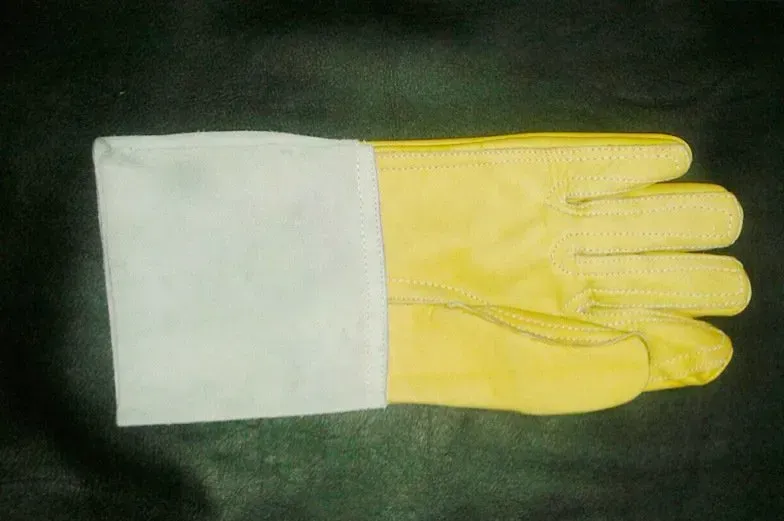 Un guante de trabajo de cuero amarillo con puño de seguridad de lona blanca, aislado sobre un fondo oscuro.