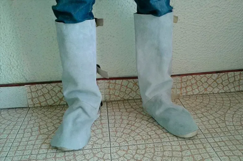 Una persona que lleva polainas altas de cuero gris claro sobre los zapatos y las espinillas, está de pie sobre un suelo de baldosas.