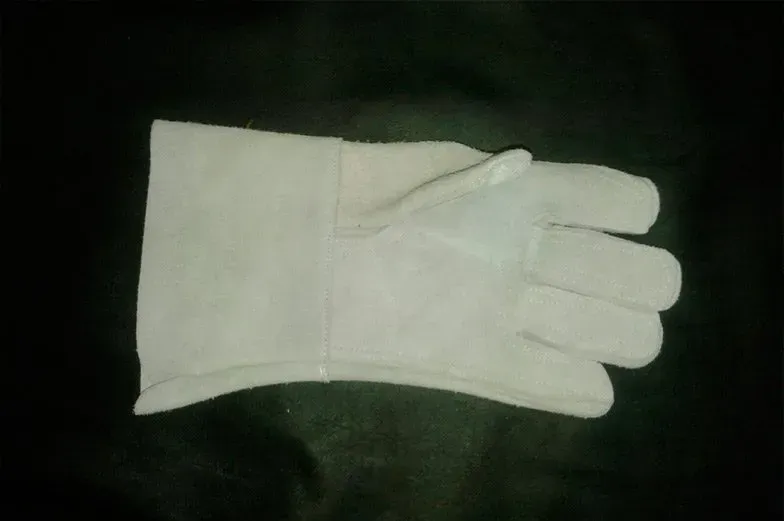 Un guante de trabajo de cuero resistente de color claro, extendido sobre un fondo negro.