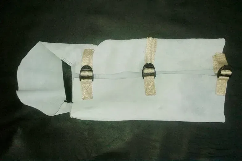 Una bata rectangular de tela blanca con tres correas ajustables de cincha beige con hebillas de plástico negras.