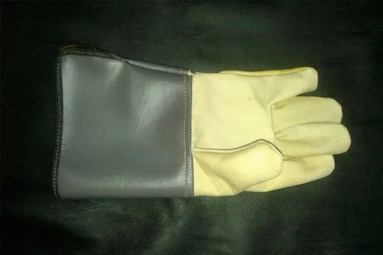 Un guante de trabajo de puño largo con un puño de cuero gris y una mano de gamuza color crema sobre un fondo negro.