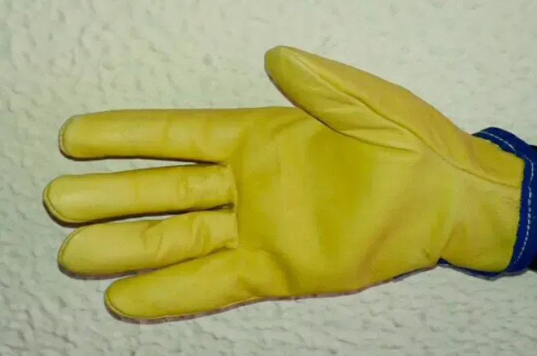 Un guante de trabajo amarillo, mostrado con la palma hacia arriba sobre un fondo texturizado de color claro.