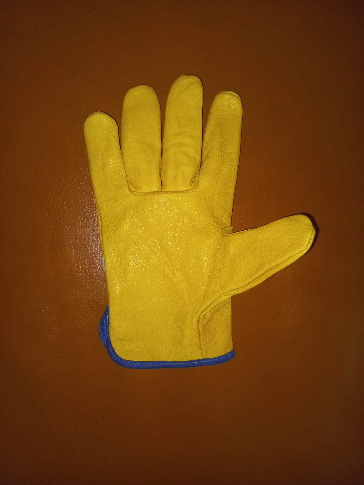 Una mano que lleva un guante de trabajo de cuero amarillo con un puño protector blanco largo, sobre un fondo rojo texturizado.