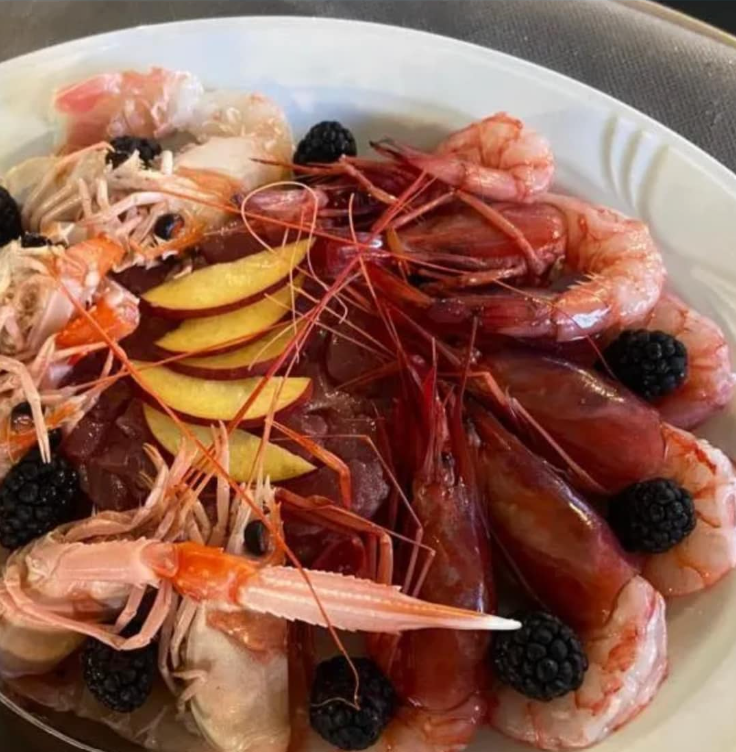 Piatto di frutti di mare: gamberi, scampi, more, fette di pesca, su piatto bianco.