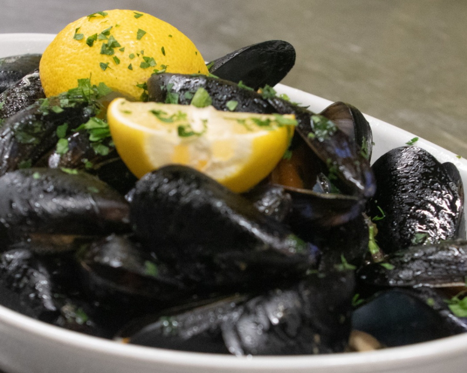 Ciotola di cozze al vapore, guarnita con limone e prezzemolo.
